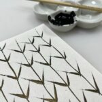 abstract marks marks on washi painted with Chinese Black Gold ink with porcelain flower dish and sumi brush in background