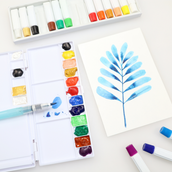 Painting of abstract watercolor leaves surround by NNC15 open box, palette with NNC15 colors squeezed into trays, and 3 tubes of NNC15 colors