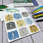 two pages with watercolor doodles of leaves on a table surrounded by watercolor pencils, a waterbrush, paper pads and a drawing pen