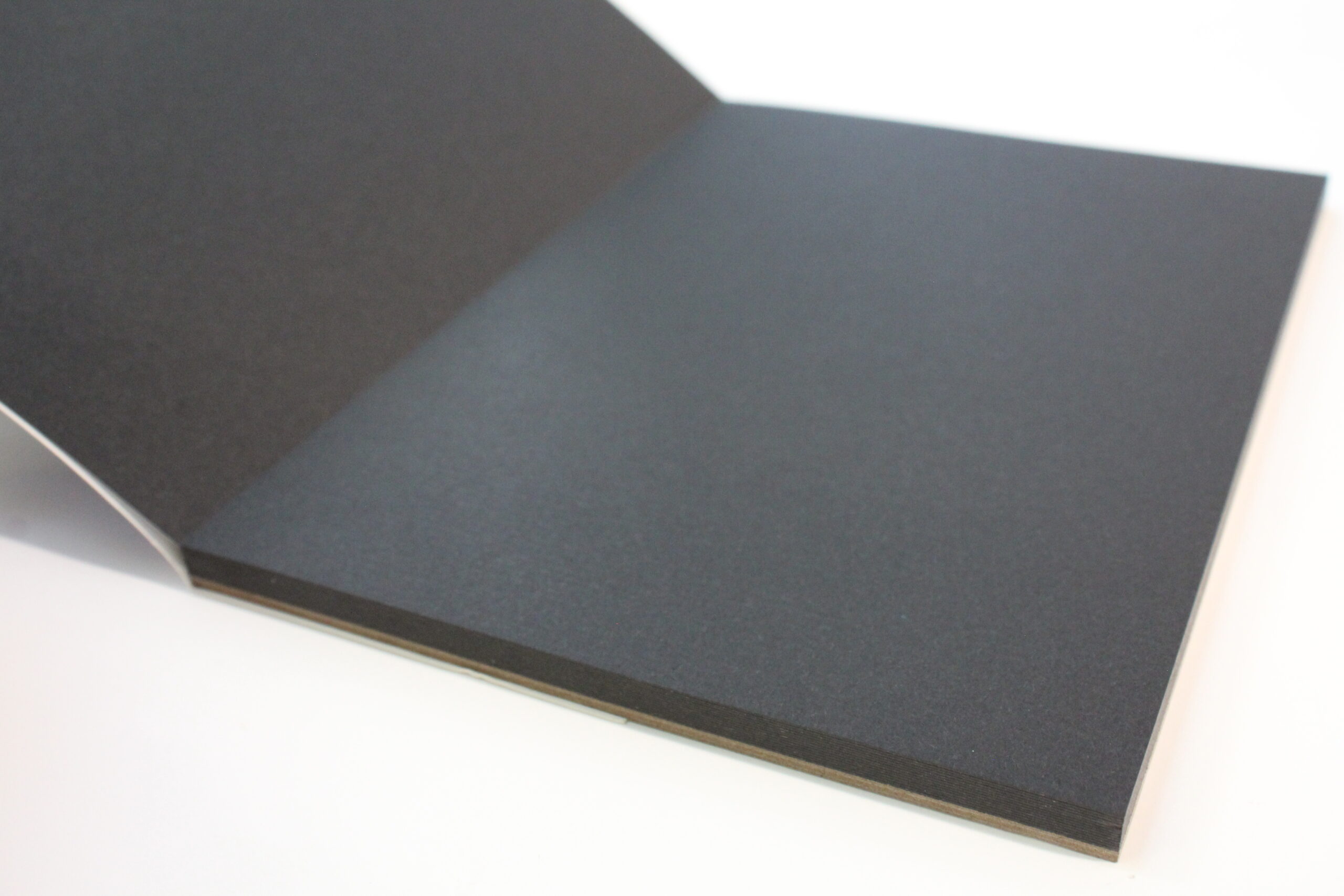 angled photo of niji black watercolor paper pad open and showing black paper sheets inside
