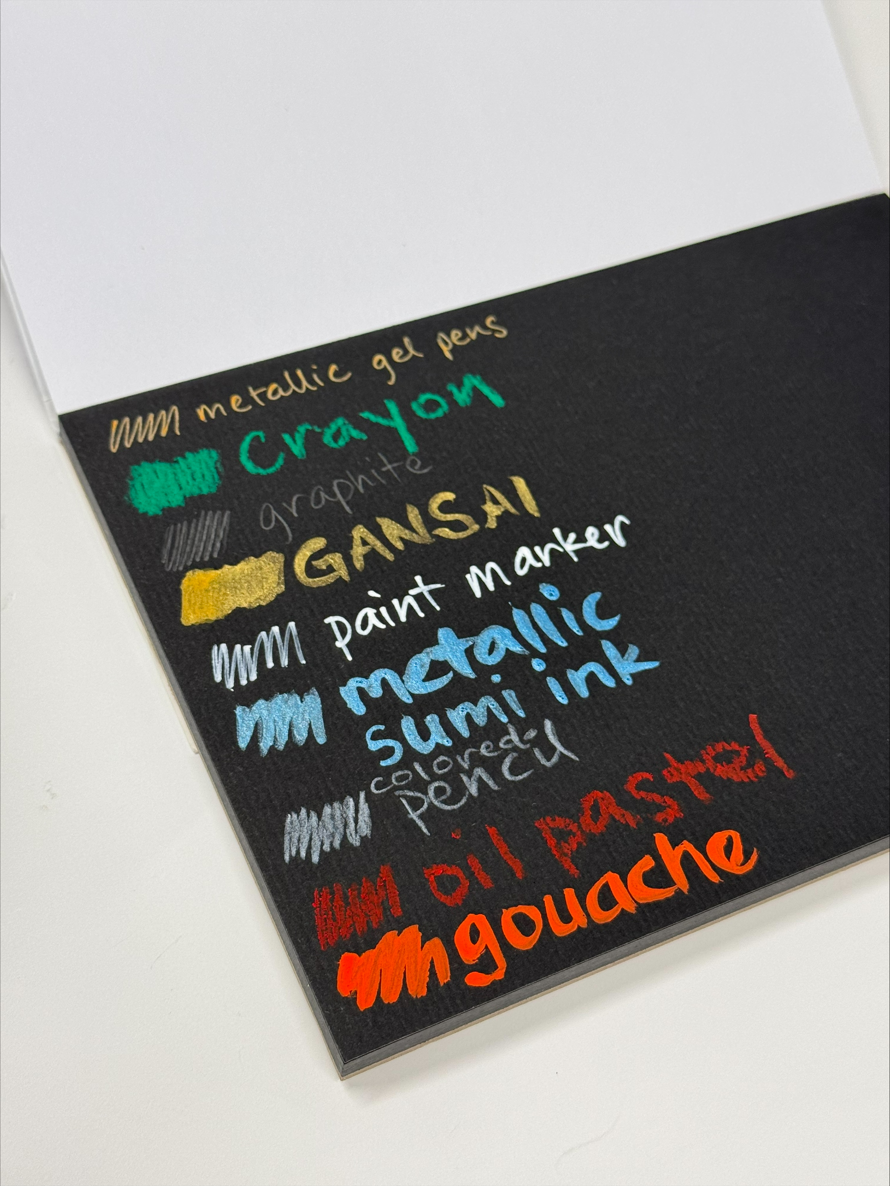 photo at an angle of swatches of various mediums on niji black watercolor paper