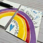 watercolor rainbow across two artist trading cards with a quote reading "the rainbow is a promise" with a Detail Master Pigment liner pen to the side