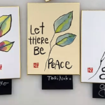 three postcard sized shikishi boards painted with etegami leaves and quotes, reading "Feel the wind in your hair," "Let there be peace" and "grow"