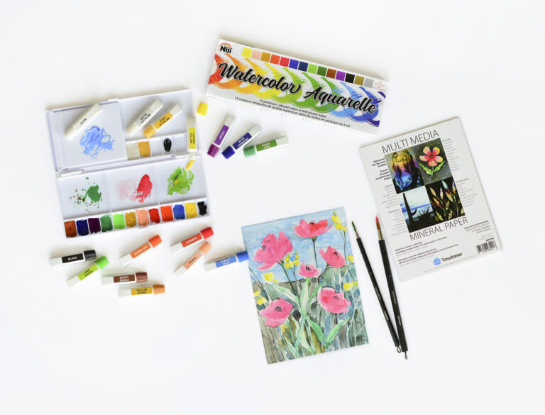 picture of the exploring watercolor kit contents: Niji Premium Watercolors, 15 colors; 6" x 8" mineral paper pad; two Fusion brushes; fold up palette with paint in trays and paint tubes around it; and a watercolor flower painting