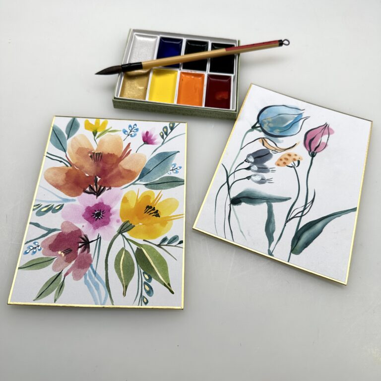 two floral gansai paintings on shikishi boards next to an 8 color gansai set and a Wa Fude brush