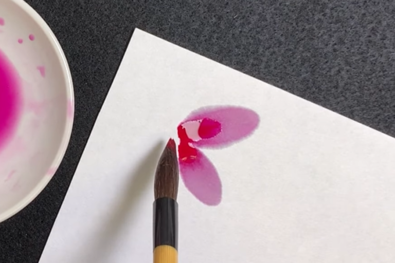 paintbrush being used to make petal marks on Hosho paper with a gansai paint and porcelain dish with paint to the side