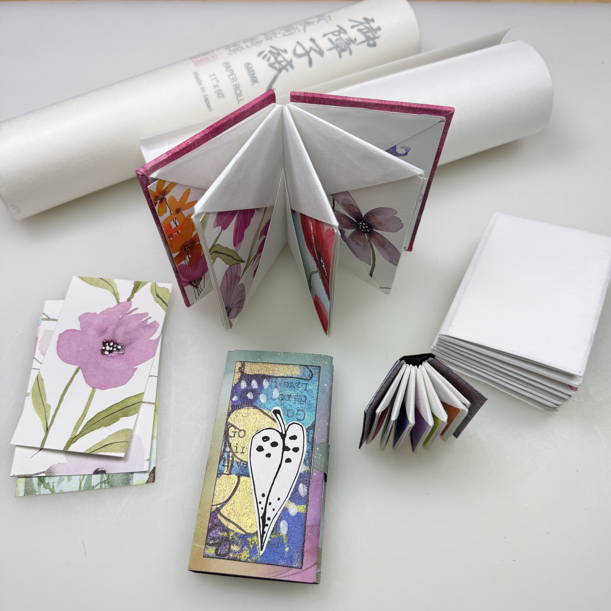 small folded origami books, watercolor florals cards, and washi paper rolls in the background