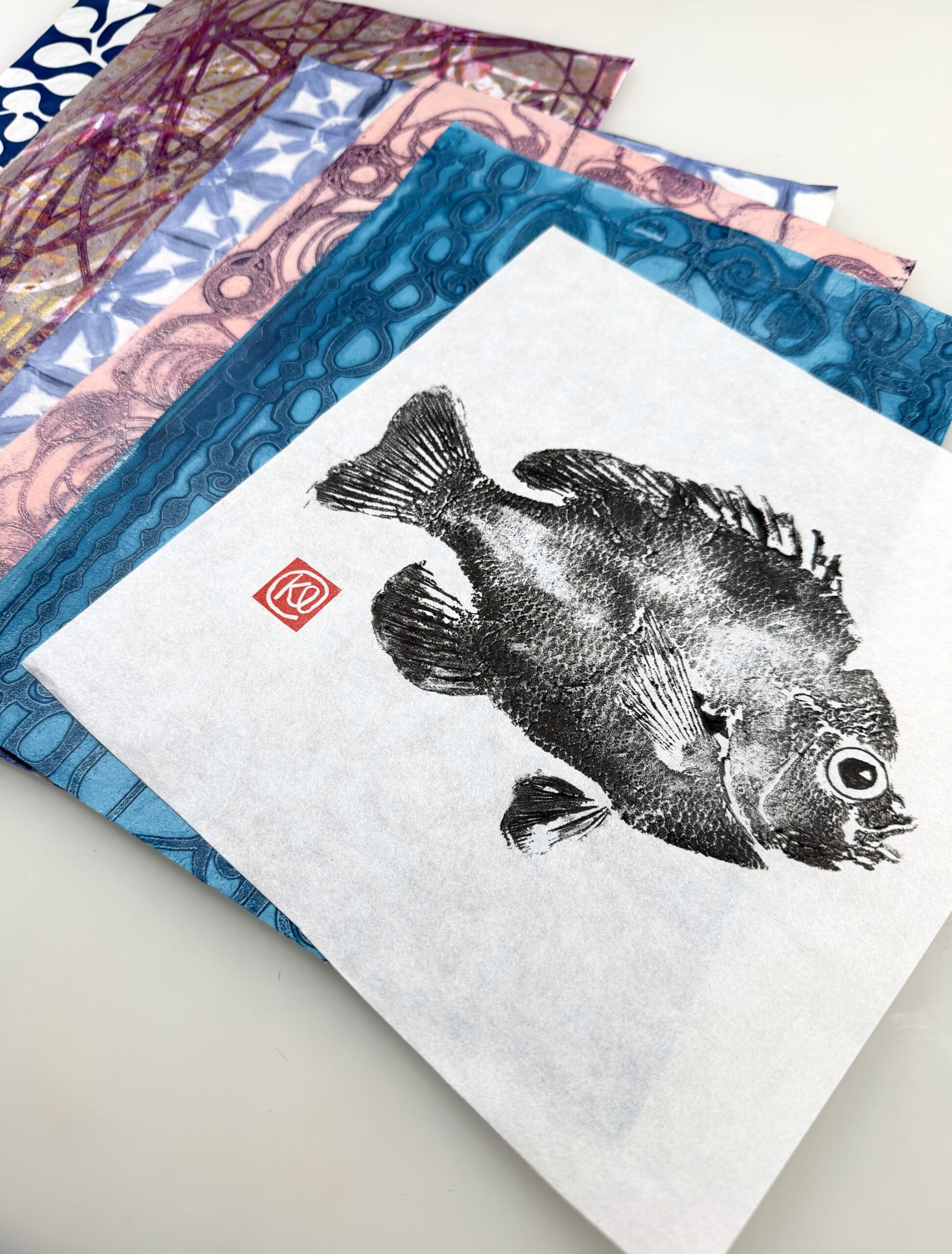 spread of colorful printed washi papers with a gyotaku fish print on top