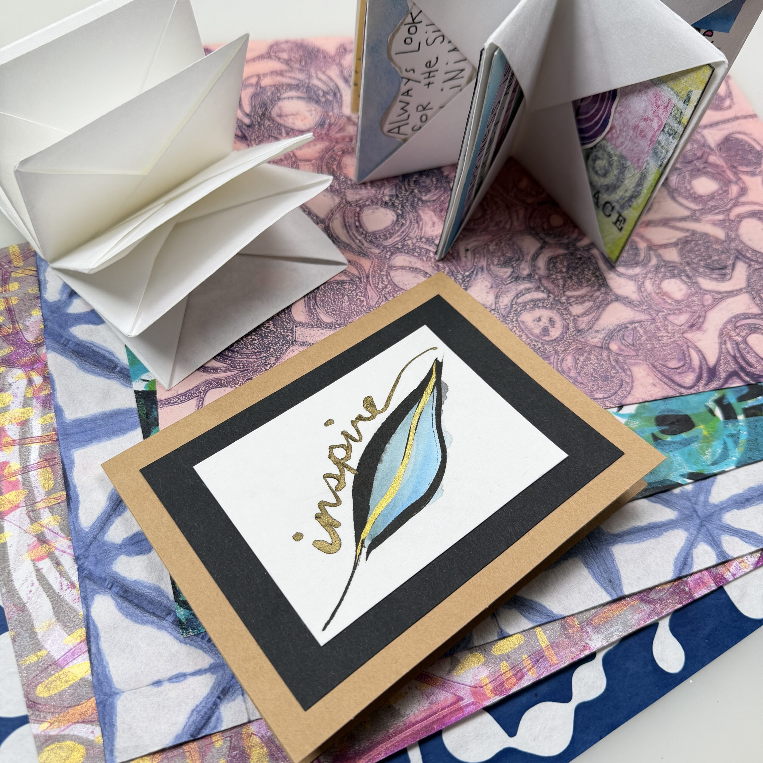 spread of colorful printed papers with a painted card and two folded books arranged on top
