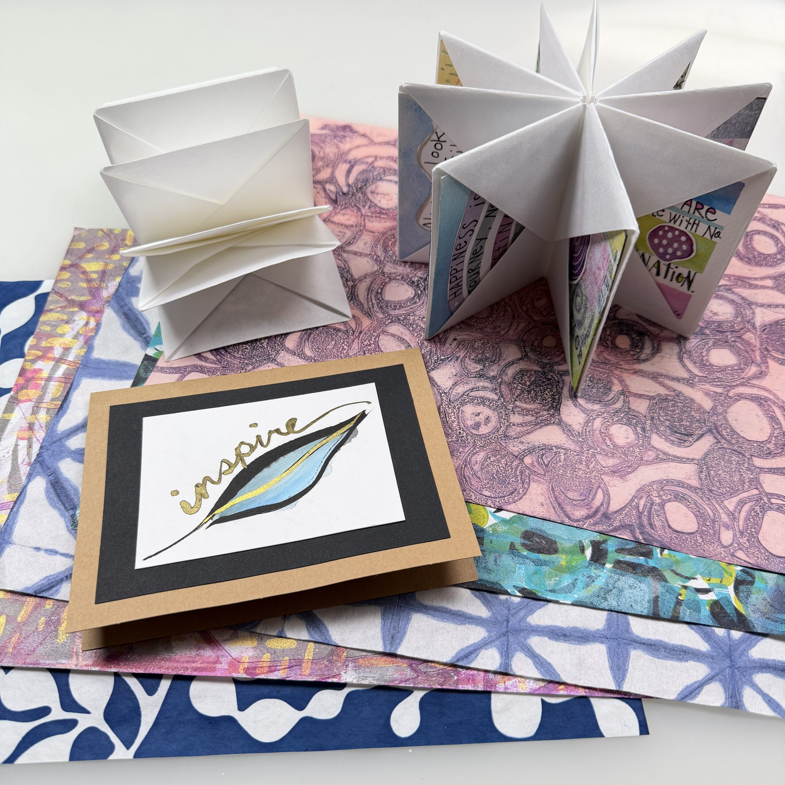 spread of colorful printed papers with a painted card and two folded books arranged on top