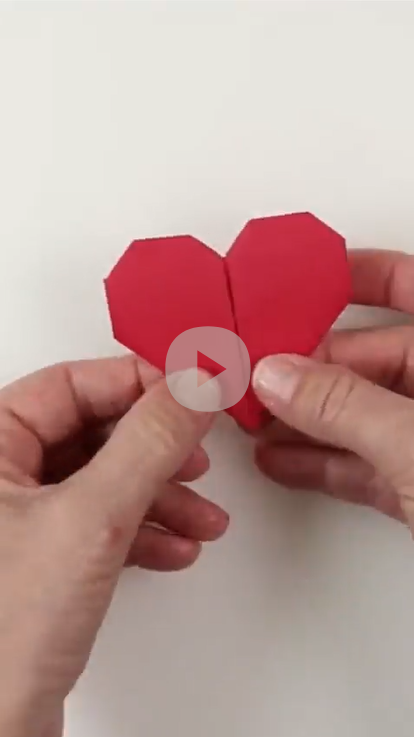 screenshot of a video showing two hands holding a red origami heart